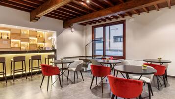 A modern bar area with wooden beams, a bar counter with stools, and round tables with red chairs.