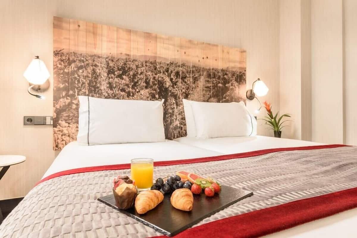 Une chambre d’hôtel avec un lit, un plateau de petit-déjeuner et deux lampes fixées au mur.
