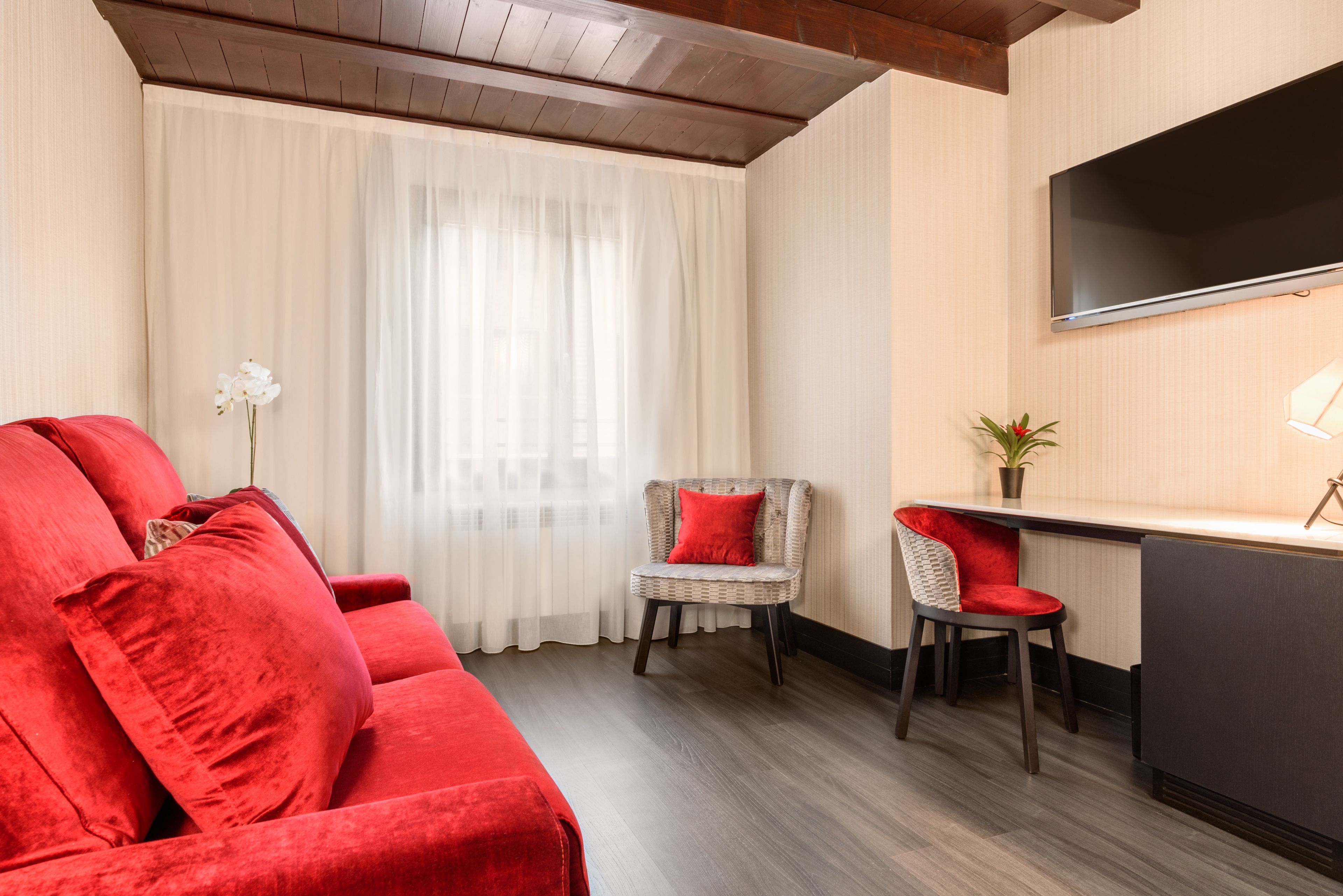 Un salón moderno con un sofá rojo, una silla de mimbre, un escritorio pequeño y un televisor montado en la pared.