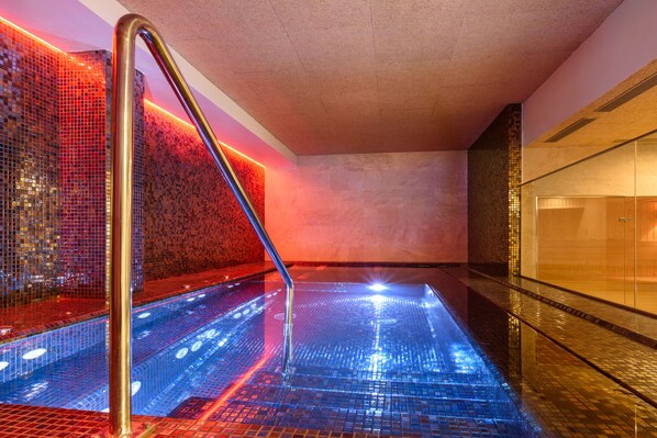 Zona de piscina interior moderna con suelo reflectante y barandilla metálica.