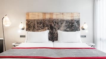 A neatly made bed with a red and gray blanket, two white pillows, and a headboard with a nature-themed artwork. There are two bedside lamps on either side of the bed.