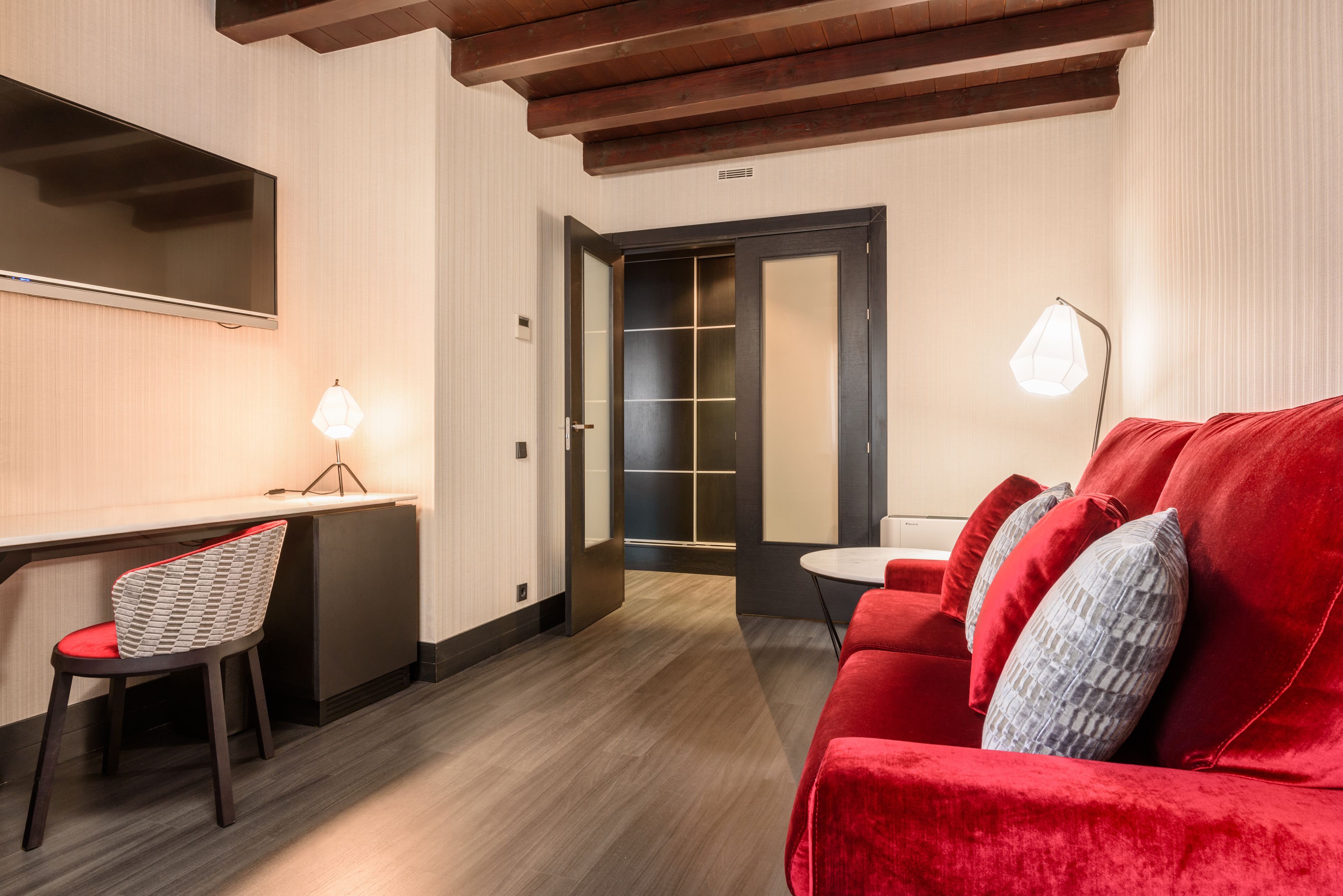 Une chambre d’hôtel moderne avec un plafond en bois, un canapé rouge, une petite table et un bureau avec une chaise.