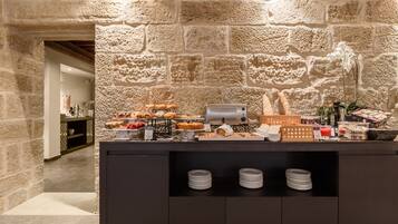 A buffet area with a stone wall backdrop, various food items, and neatly stacked plates.