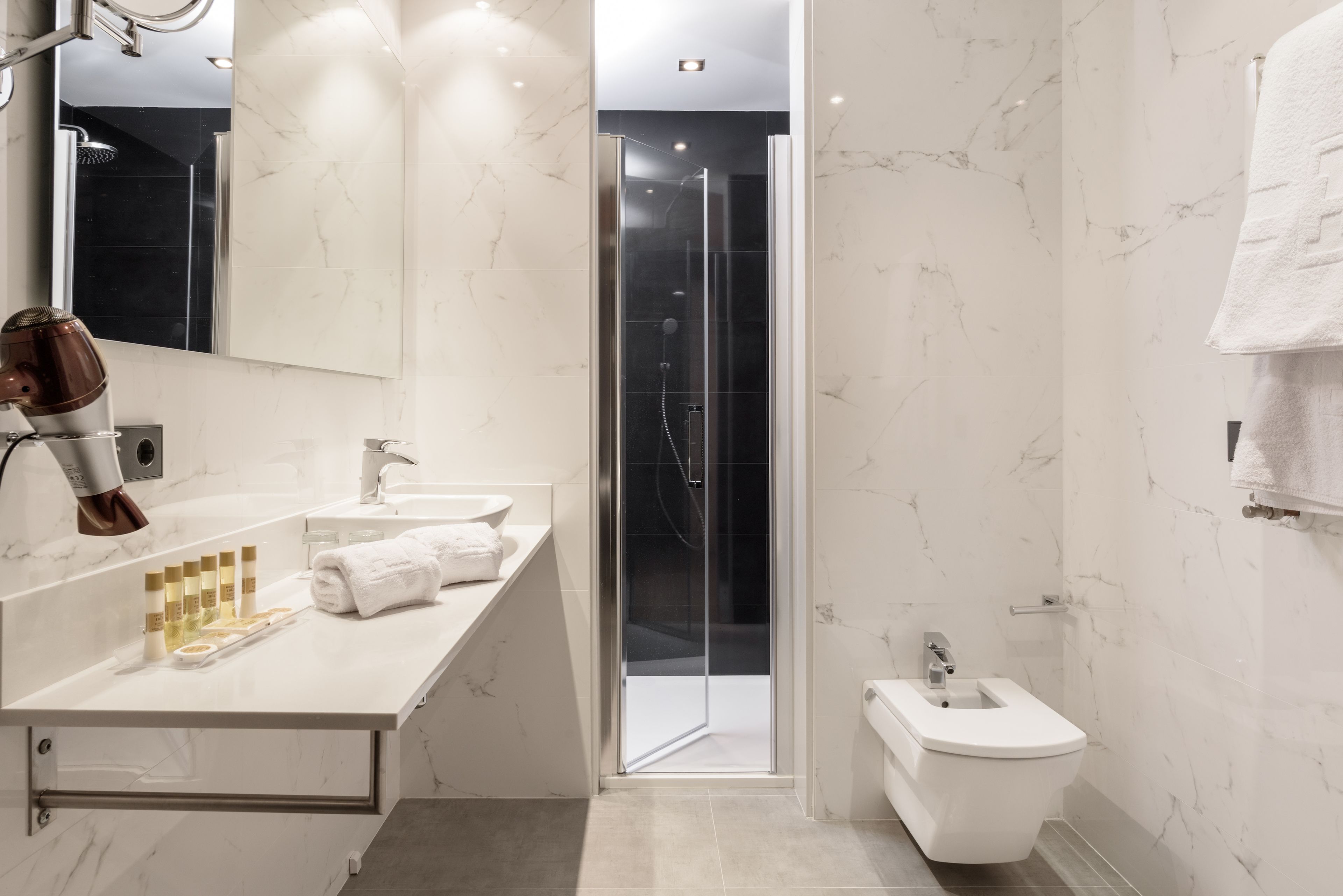A modern bathroom with a marble countertop, a glass shower enclosure, and a bidet.