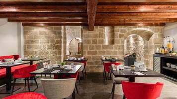 A restaurant with stone walls, wooden beams, and red chairs. Tables are set with plates, glasses, and cutlery.