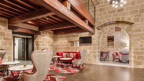 Un vestíbulo amplio con paredes de piedra, vigas de madera y una zona de estar moderna con mobiliario rojo y blanco.
