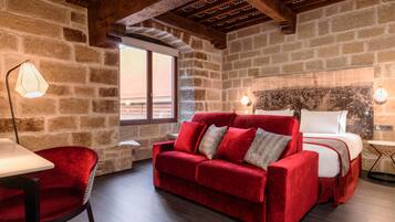 A cozy room with a red sofa, a bed, and a stone wall.