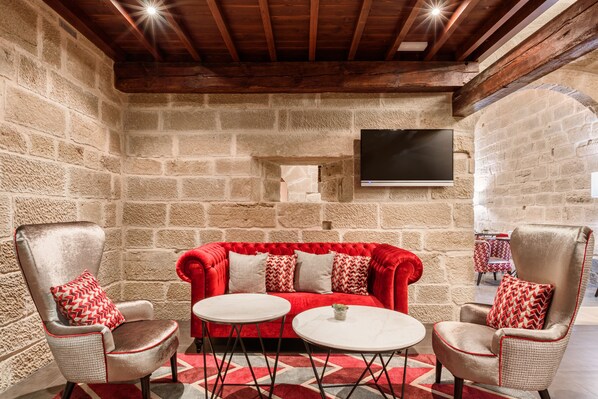 Una habitación acogedora con un sofá rojo, dos sillones y un televisor montado en la pared.