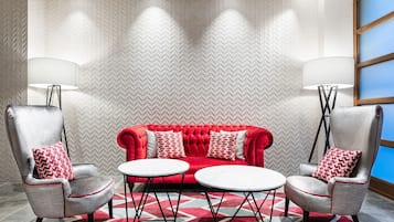 Una habitación moderna con un sofá rojo, dos sillones y una mesita.