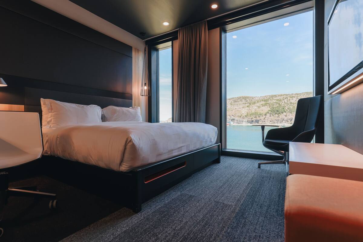 A modern hotel room with a large bed, a desk, and a view of the desert landscape.