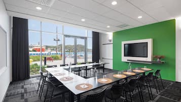 A conference room with a large table, chairs, a TV, and a view of the outside.