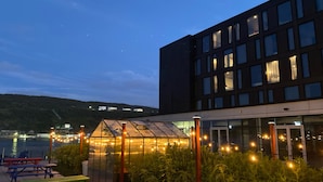 Een modern gebouw met een glazen serre en een buitenzitgedeelte met picknicktafels.