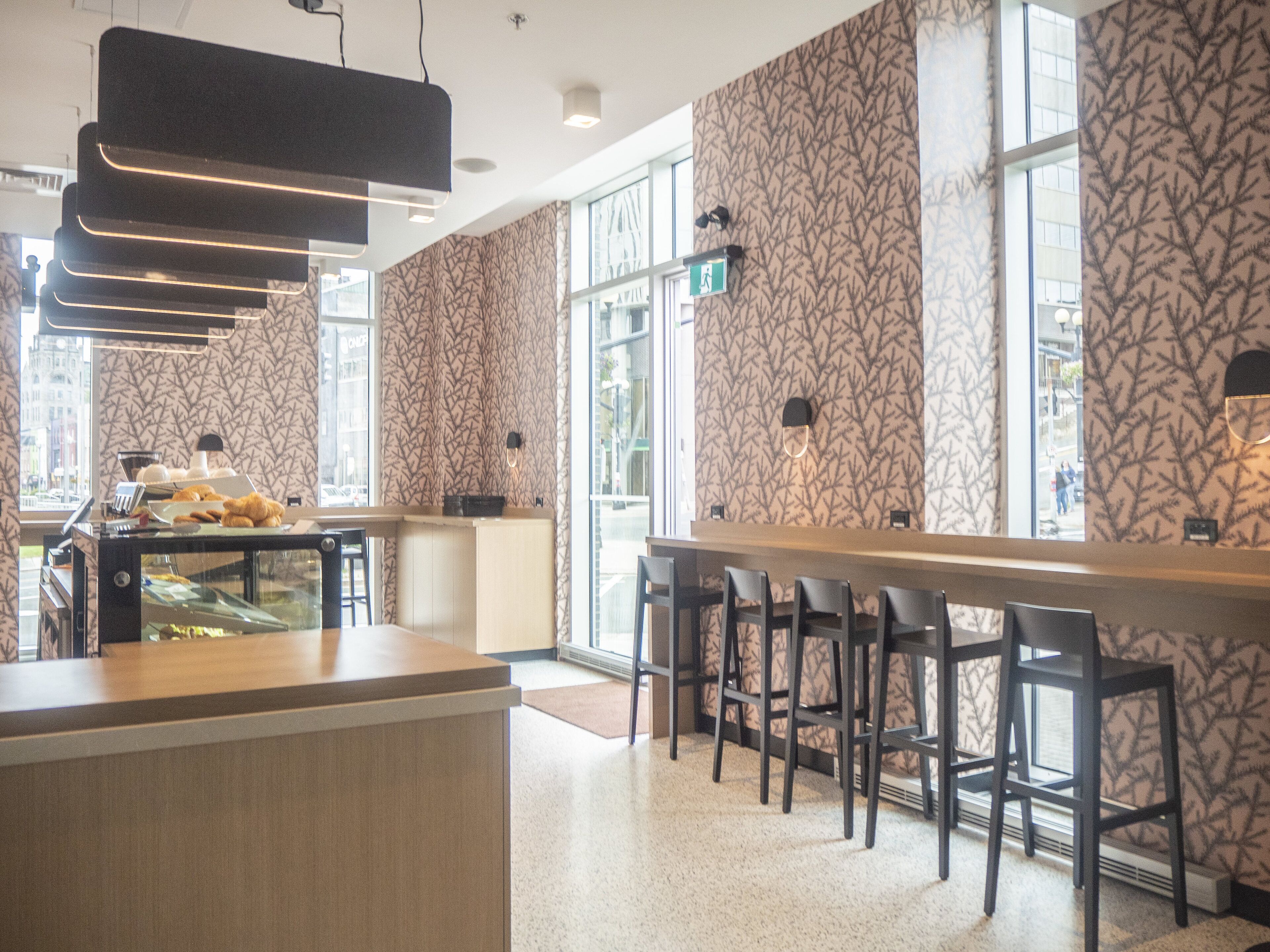 A modern bar area with a patterned wallpaper, a counter with a glass display case, and a seating area with bar stools.
