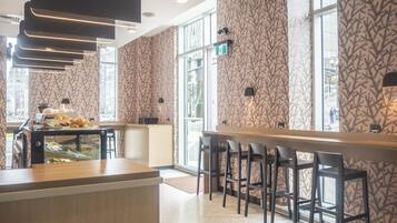 A modern bar area with a patterned wallpaper, a counter with a glass display case, and a seating area with bar stools.