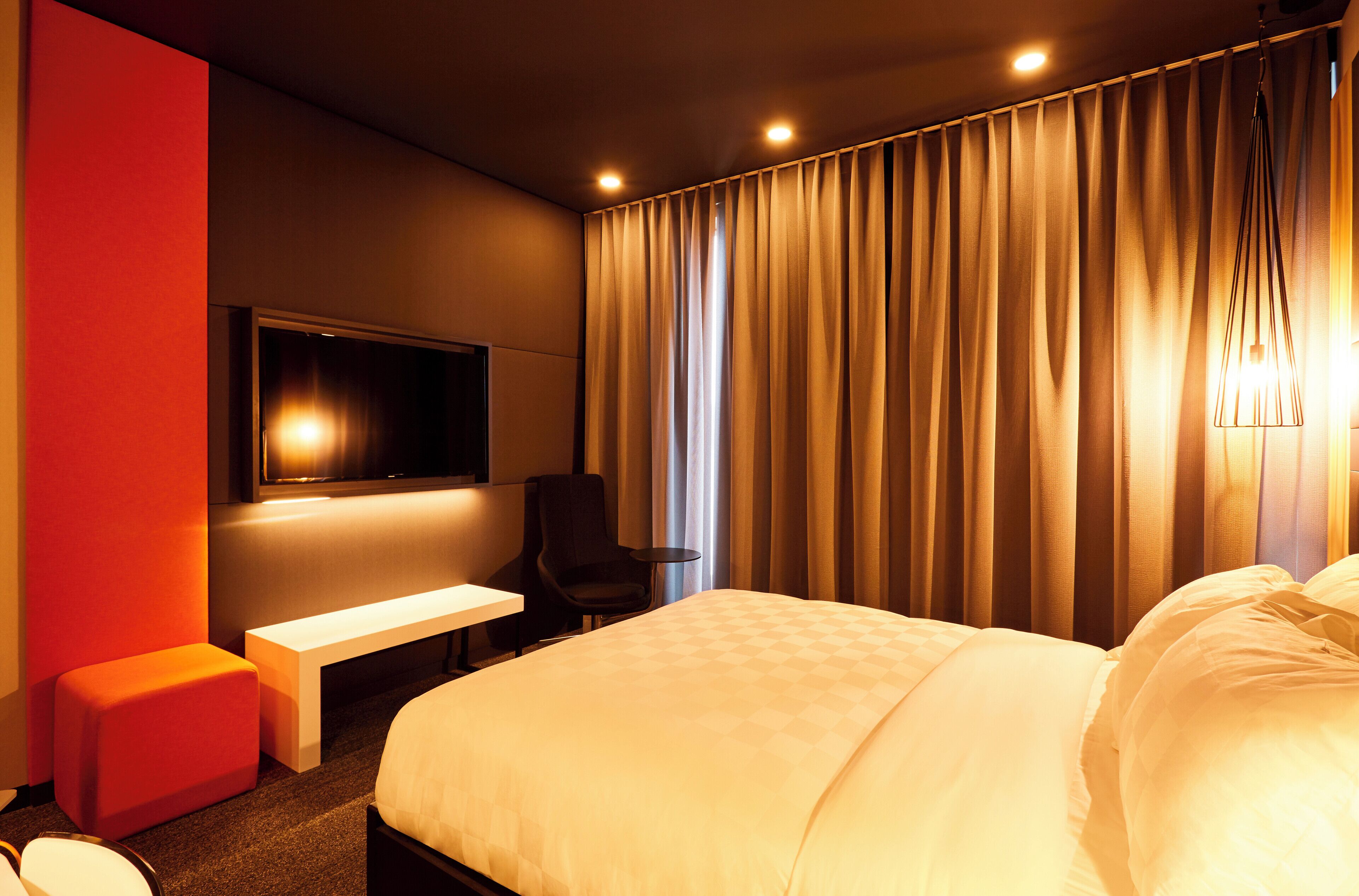 Une chambre d’hôtel équipée d’un lit, d’un bureau, d’une chaise, d’une télévision et d’une grande fenêtre avec des rideaux.
