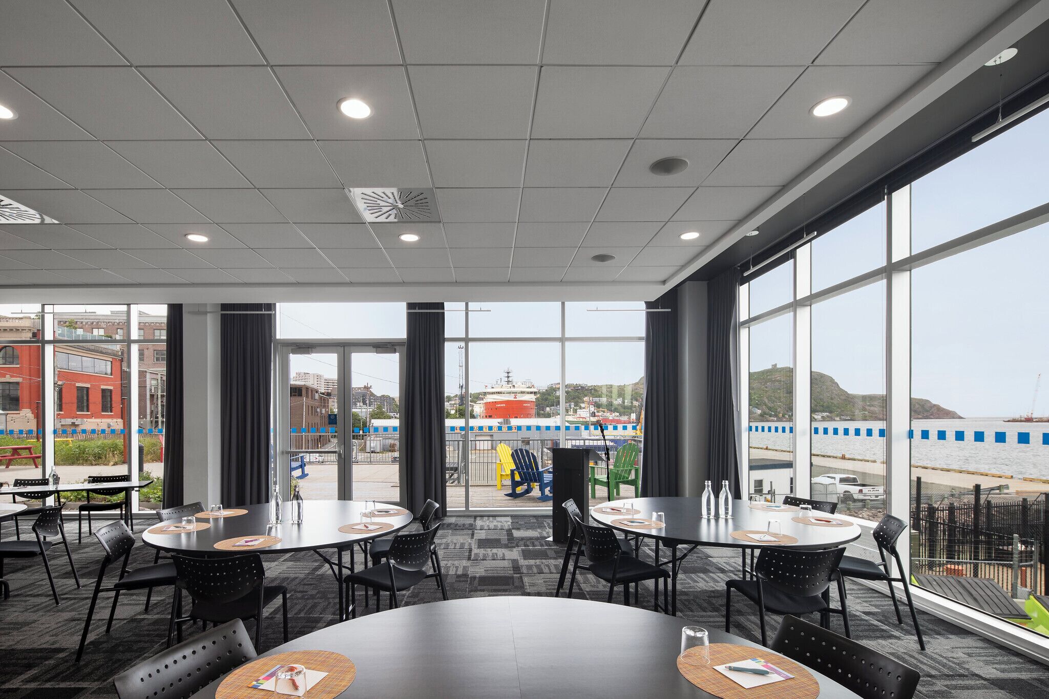 A conference room with large windows, round tables, and black chairs.
