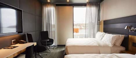 Ein Hotelzimmer mit einem Bett, einem Schreibtisch mit Stuhl, einem Fernseher und einem Fenster mit Vorhängen.