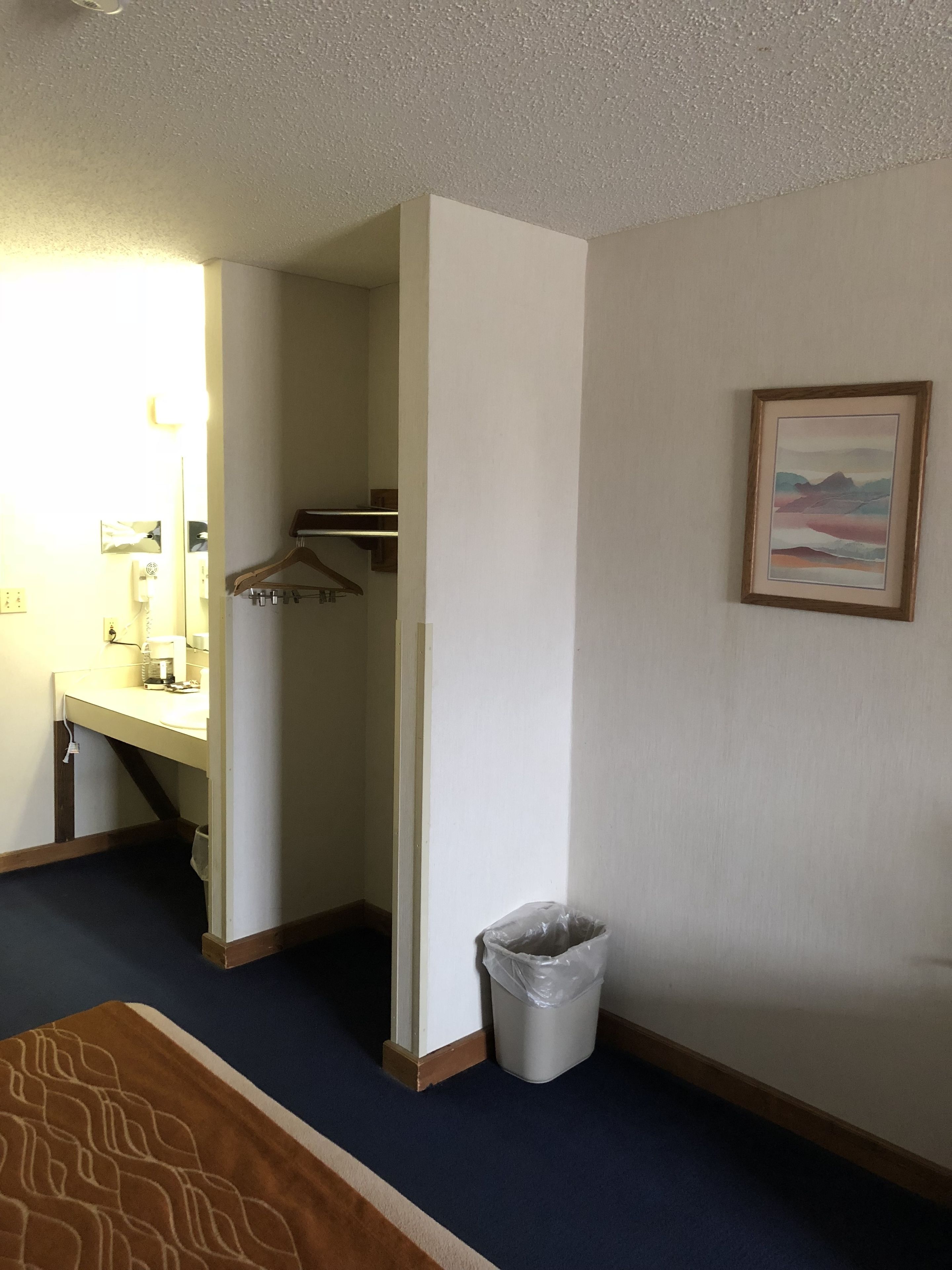 A hotel room with a bathroom, a bed, a trash bin, and a framed picture on the wall.