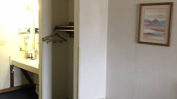 A hotel room with a bathroom, a bed, a trash bin, and a framed picture on the wall.