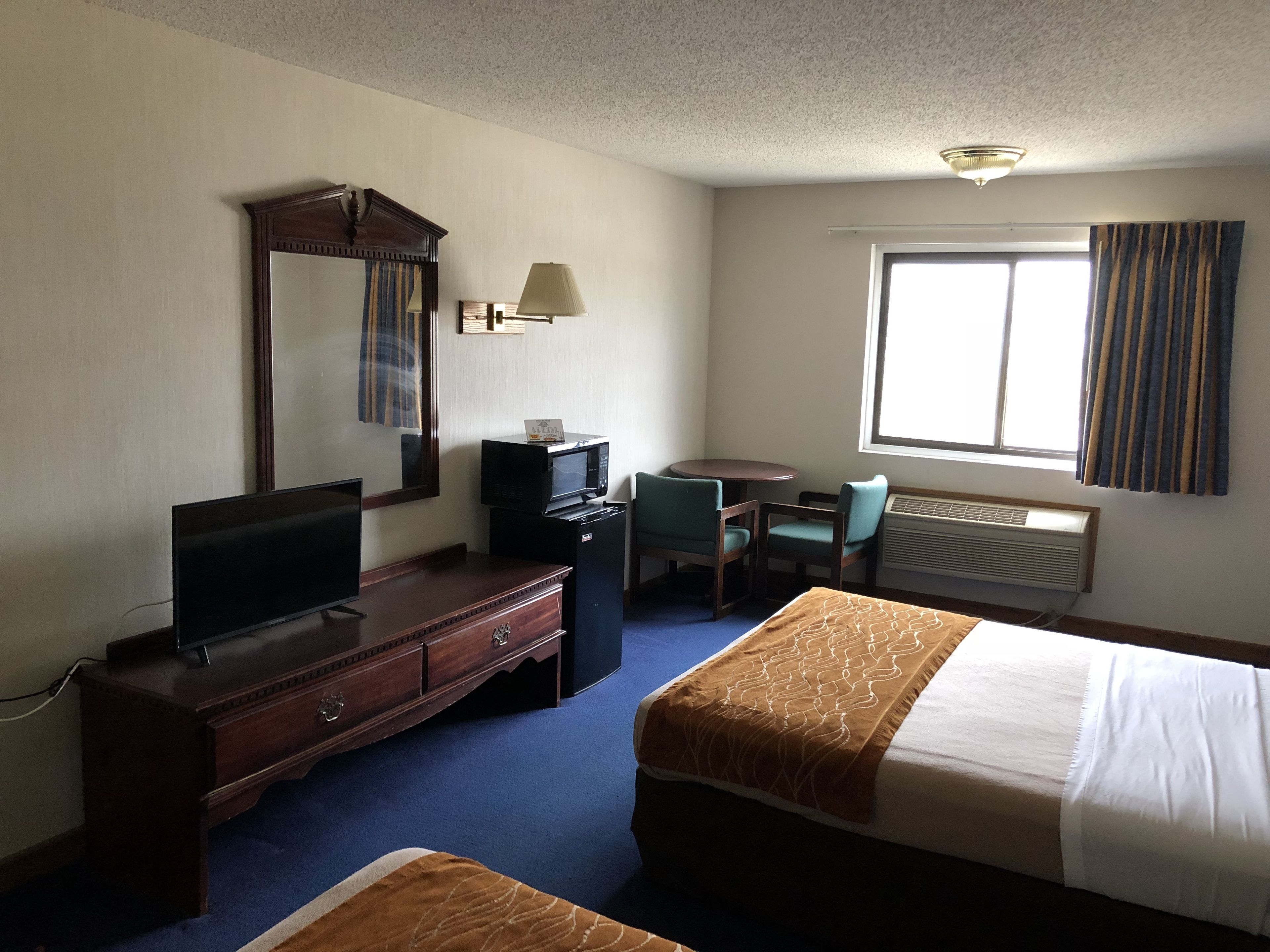 A hotel room with a bed, a desk, a chair, a television, a dresser, a mirror, and a window with curtains.