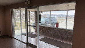 Entrada de un edificio con puertas de cristal, piso de baldosas y vista a un estacionamiento.