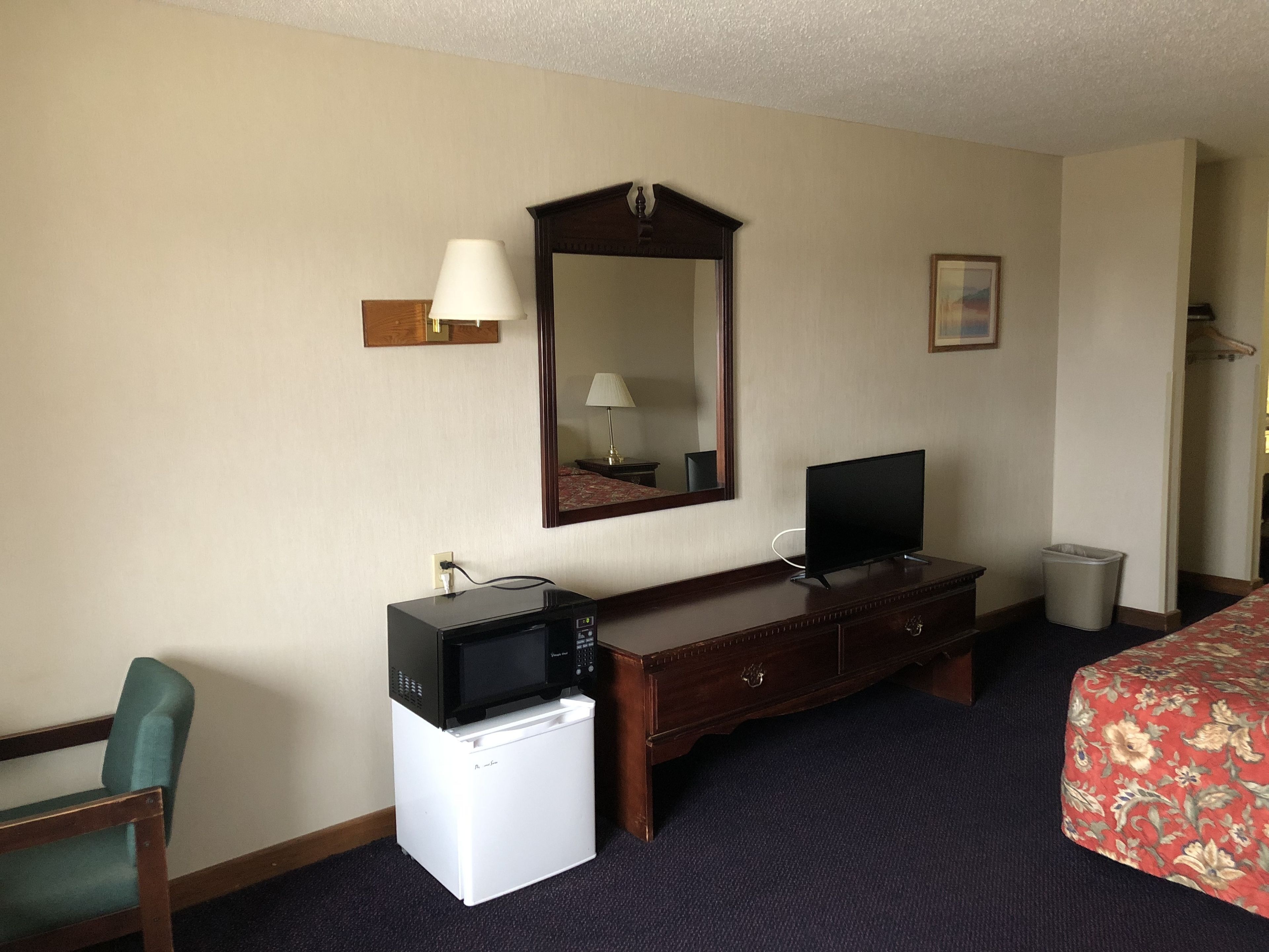 Una habitación de hotel con una cama, un escritorio con televisor, un microondas y un refrigerador pequeño.