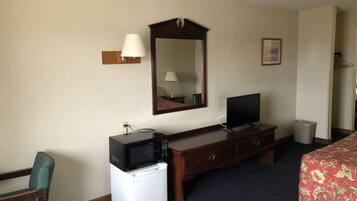 Una habitación de hotel con una cama, un escritorio con televisor, un microondas y un refrigerador pequeño.