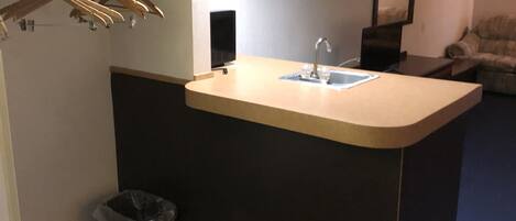 A small kitchenette with a sink, a trash can, and a coat rack.