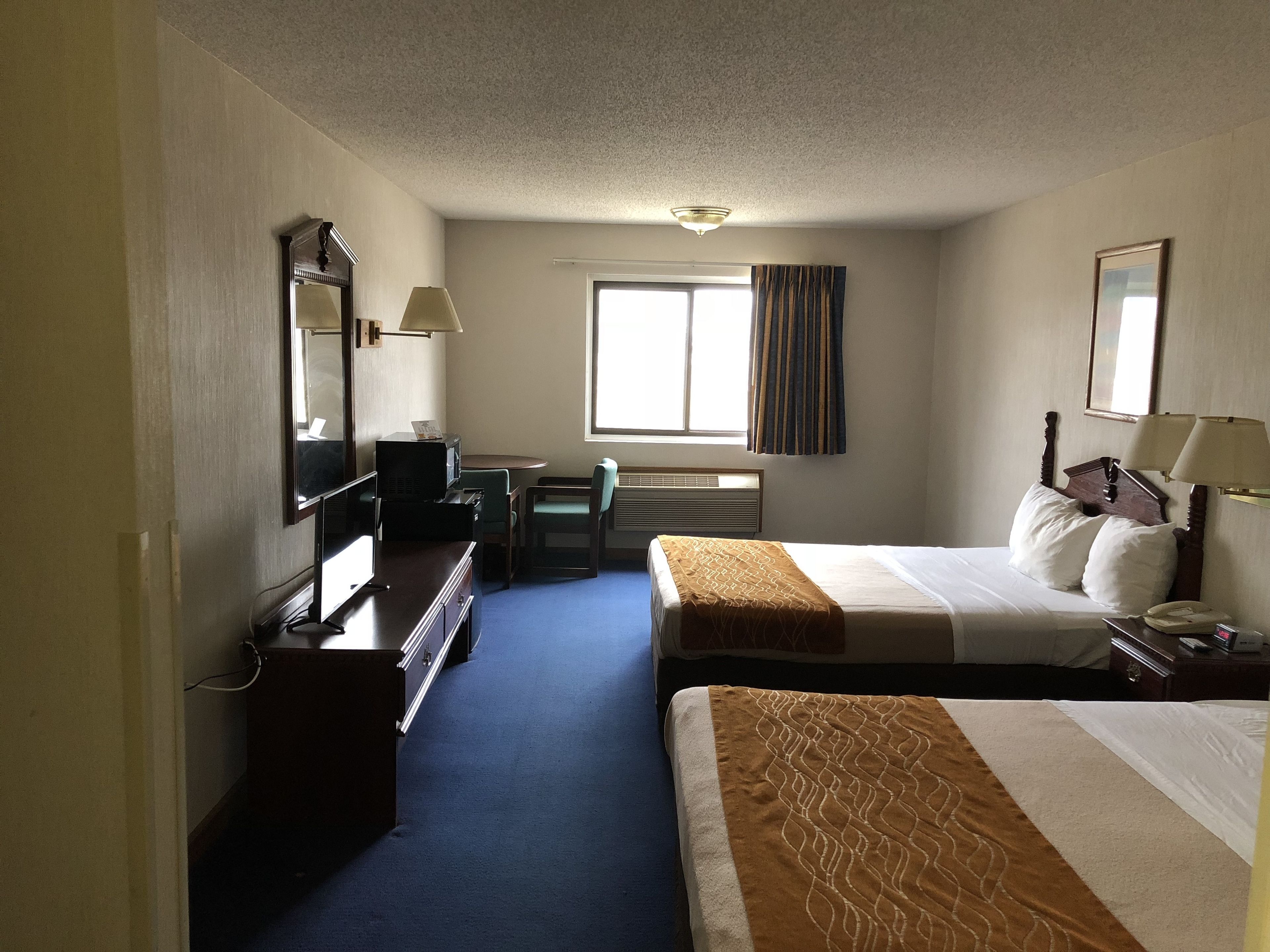 A hotel room with two beds, a desk, a chair, a TV, and a window with curtains.