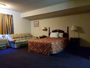 Habitación de hotel con cama, sofá, escritorio con lámpara y un cuadro en la pared.