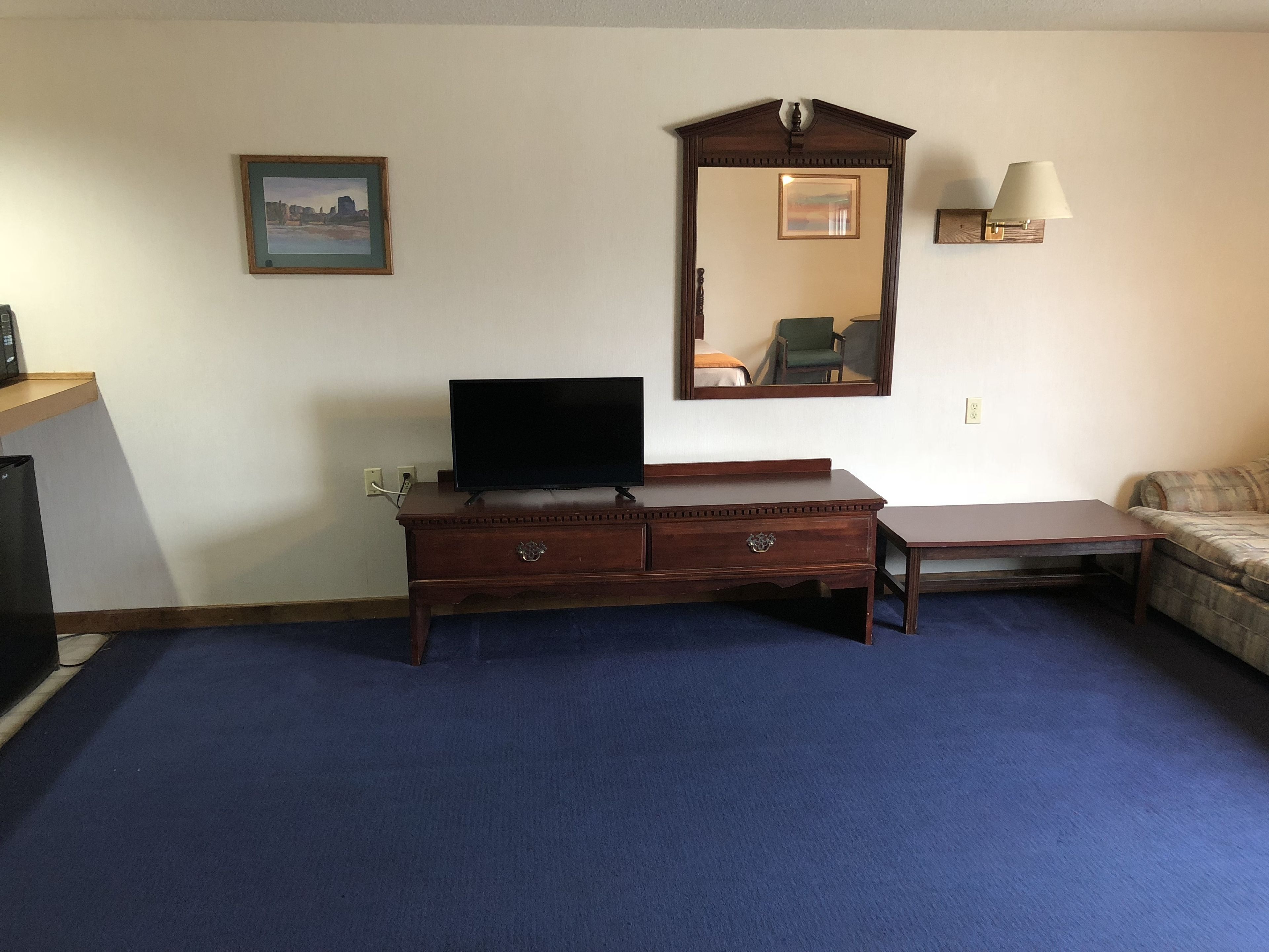 Een kamer met een houten dressoir, een flatscreen televisie, een spiegel, een lamp en een bank.