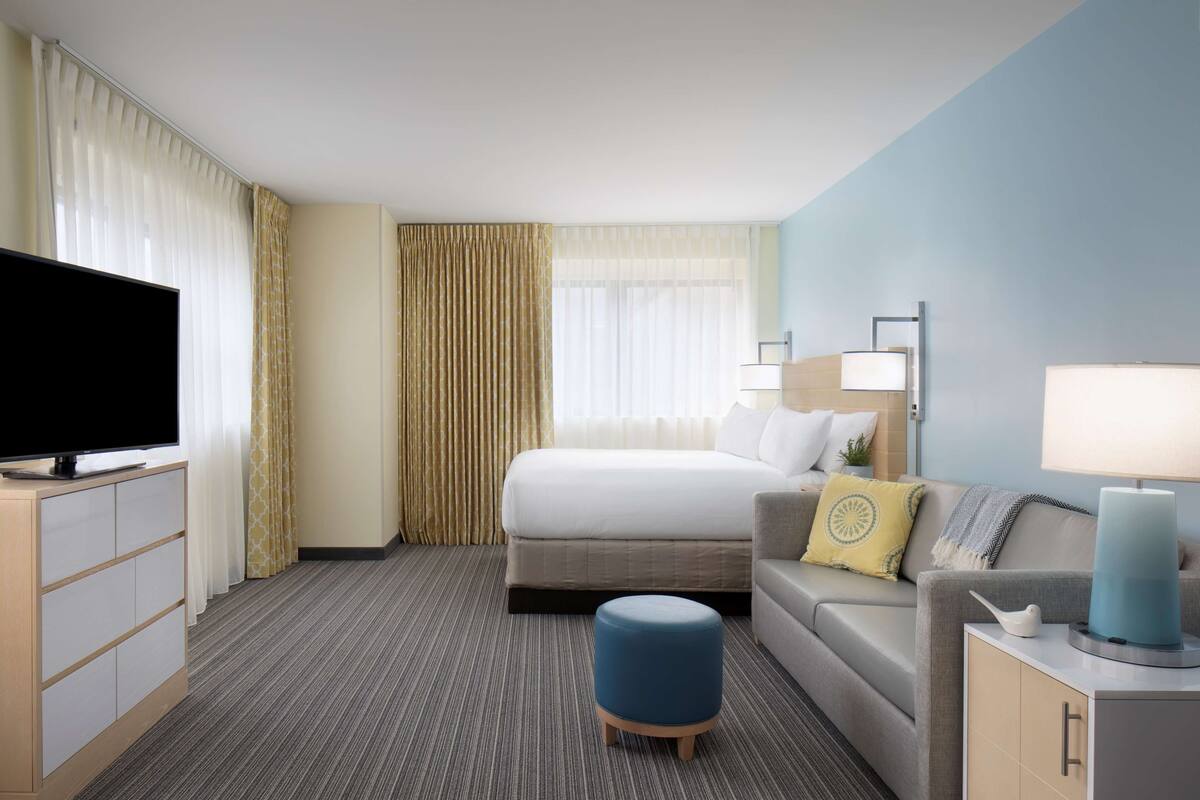 Una habitación de hotel con una cama, un sofá, un televisor y un escritorio con una lámpara.