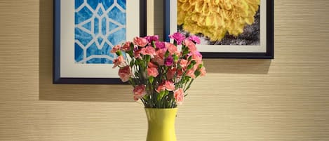 Una mesa con un jarrón amarillo de flores rosadas, dos muffins y dos vasos de jugo de naranja.