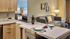 A hotel room with a dining area, kitchenette, and a bed.