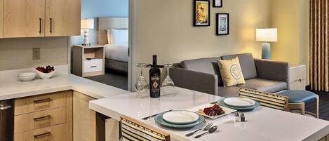 A hotel room with a dining area, kitchenette, and a bed.