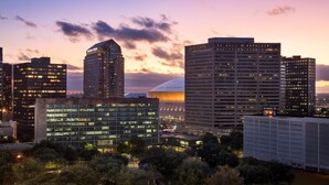 A cityscape at dusk with modern high-rise buildings, including a distinctive curved building with a dome.