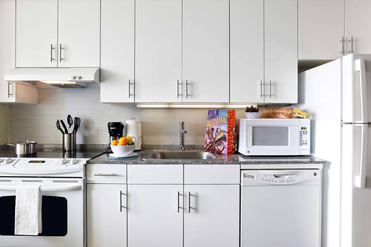 Una cocina moderna con armarios blancos, un lavamanos de acero inoxidable, un microondas, una estufa y un lavavajillas.