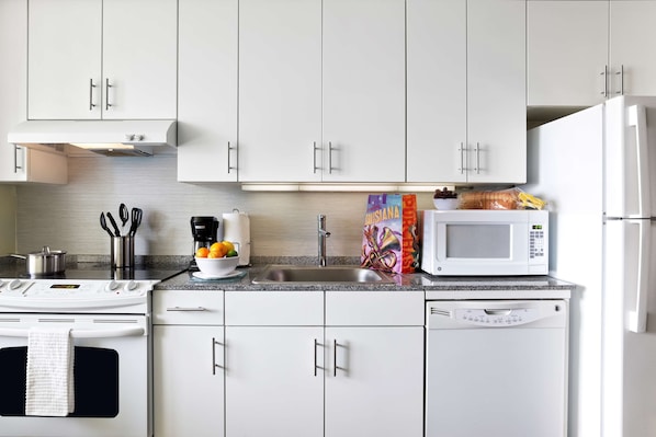 A modern kitchen with white cabinets, a stainless steel sink, a microwave, a stove, and a dishwasher.