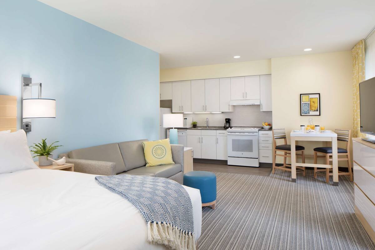 Una habitación de hotel moderna con cama, sofá, pequeña mesa de comedor y kitchenette.