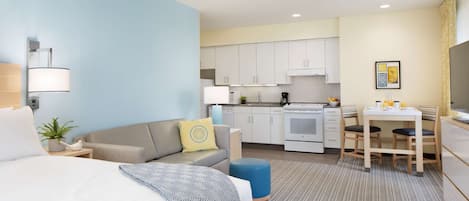 Una habitación de hotel moderna con cama, sofá, pequeña mesa de comedor y kitchenette.
