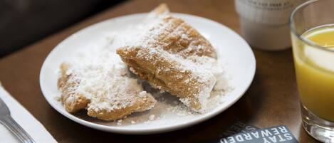 A plate with a pastry dusted with powdered sugar, a cup labeled "SONESTA," and a glass of orange juice on a table.