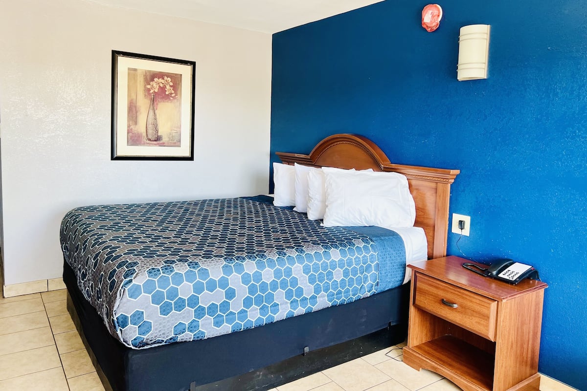 A hotel room with a bed, a nightstand with a phone, and a painting on the wall.