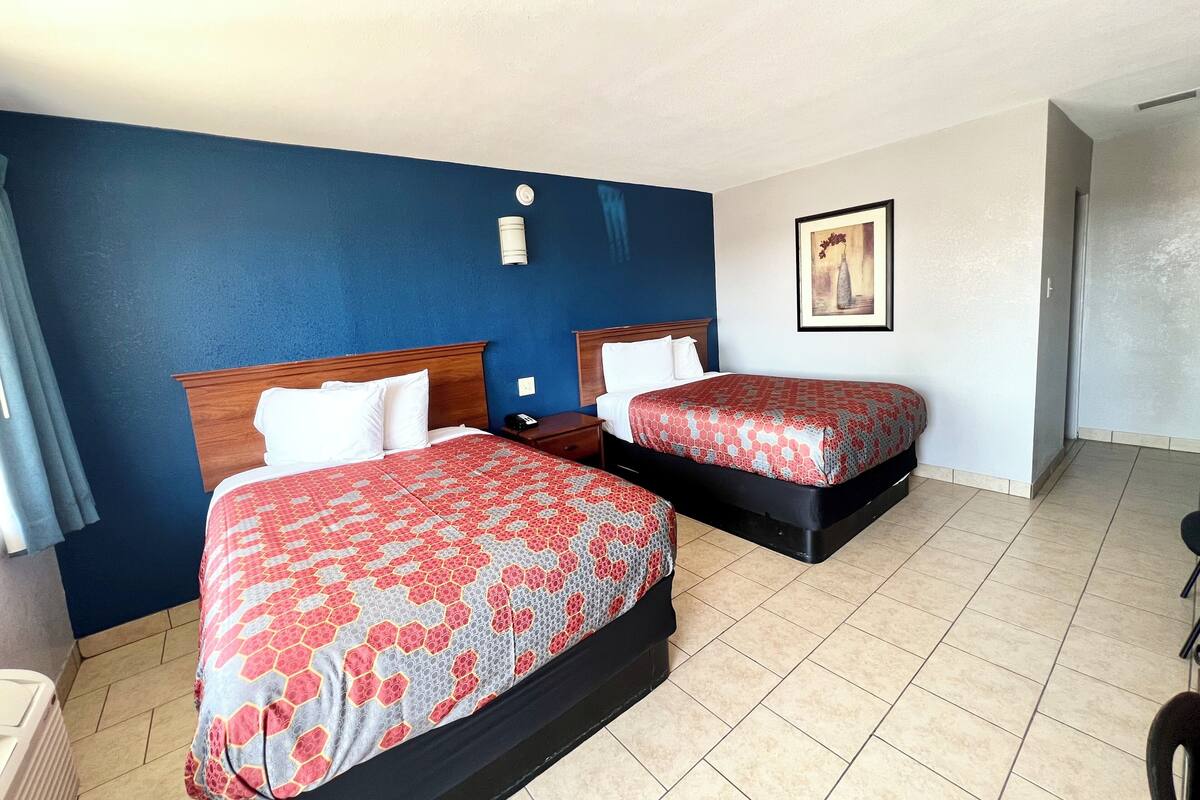 A hotel room with two beds, a nightstand, a painting on the wall, and a tiled floor.