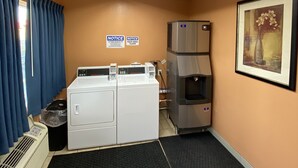 A laundry room with two washing machines, a dryer, and a water heater. There are two signs on the wall indicating the room is for laundry only.