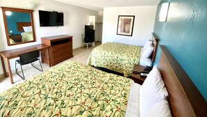 A hotel room with two beds, a desk, a dresser, a television, and a framed picture on the wall.