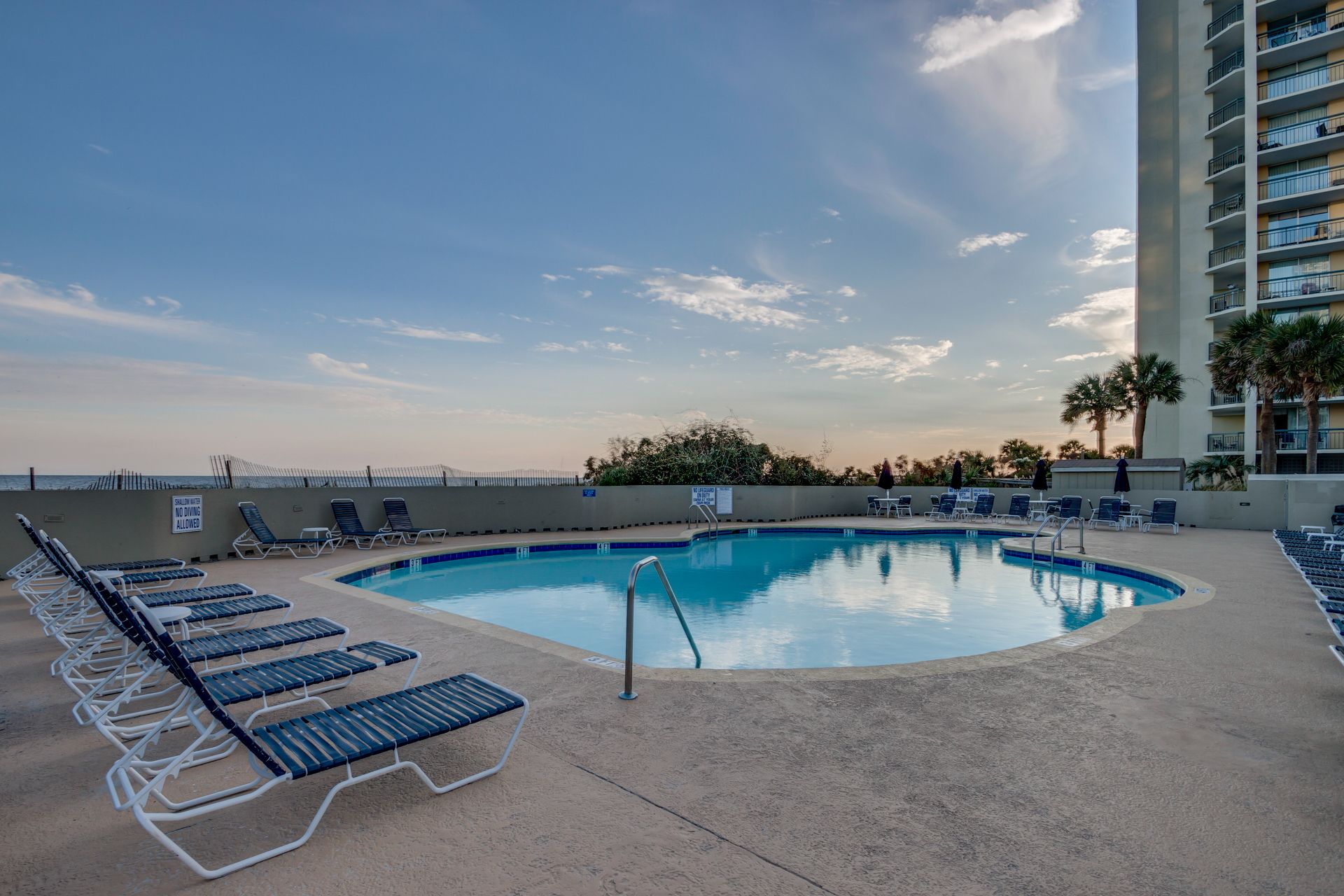 A pool area with lounge chairs and a sign indicating no diving allowed.