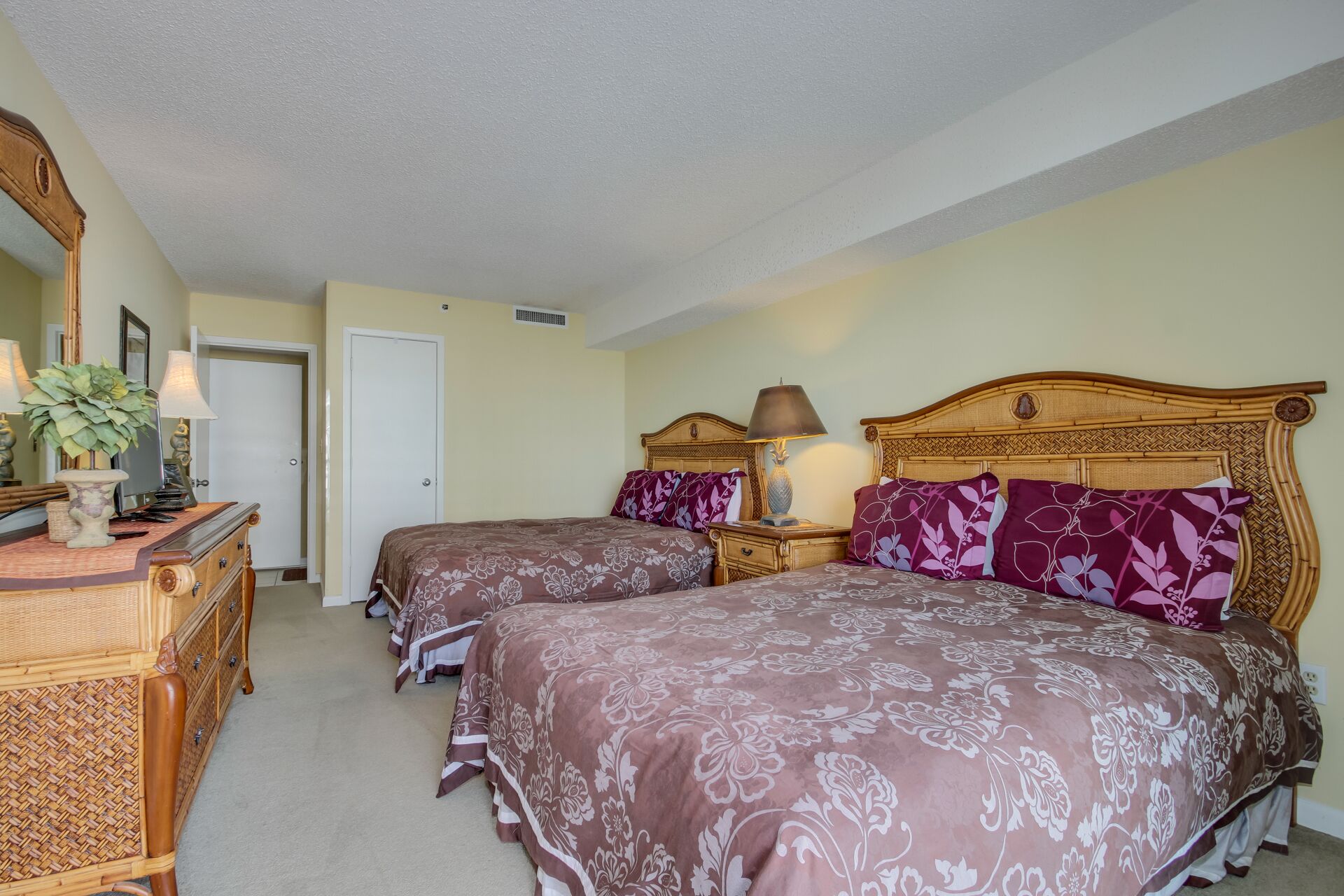 A hotel room with two beds, a wooden dresser, a mirror, and a lamp.