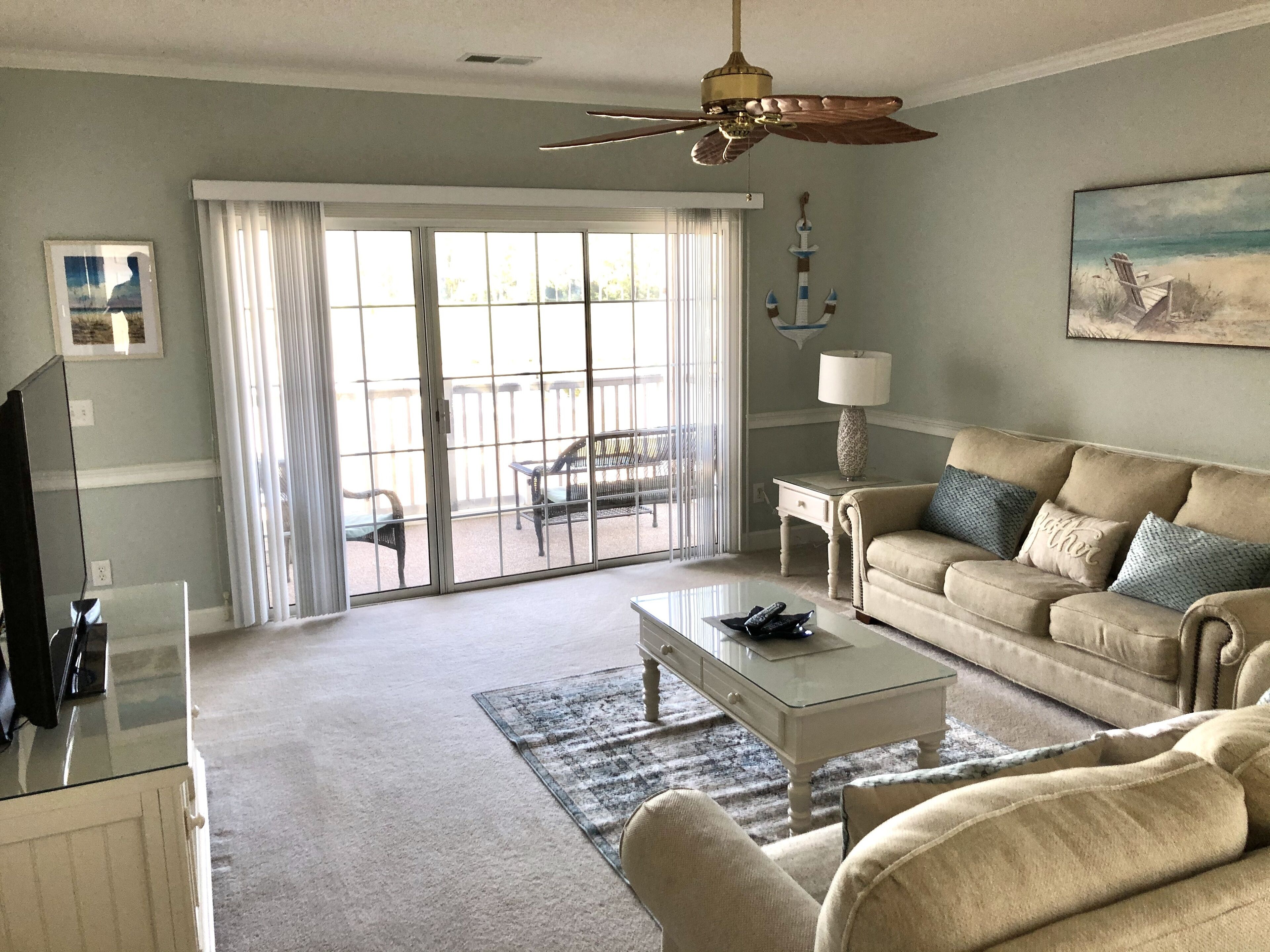 A living room with a beige sofa, a glass coffee table, and a ceiling fan.