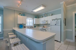 Una cocina moderna con muebles blancos, una isla central y un microondas integrado.