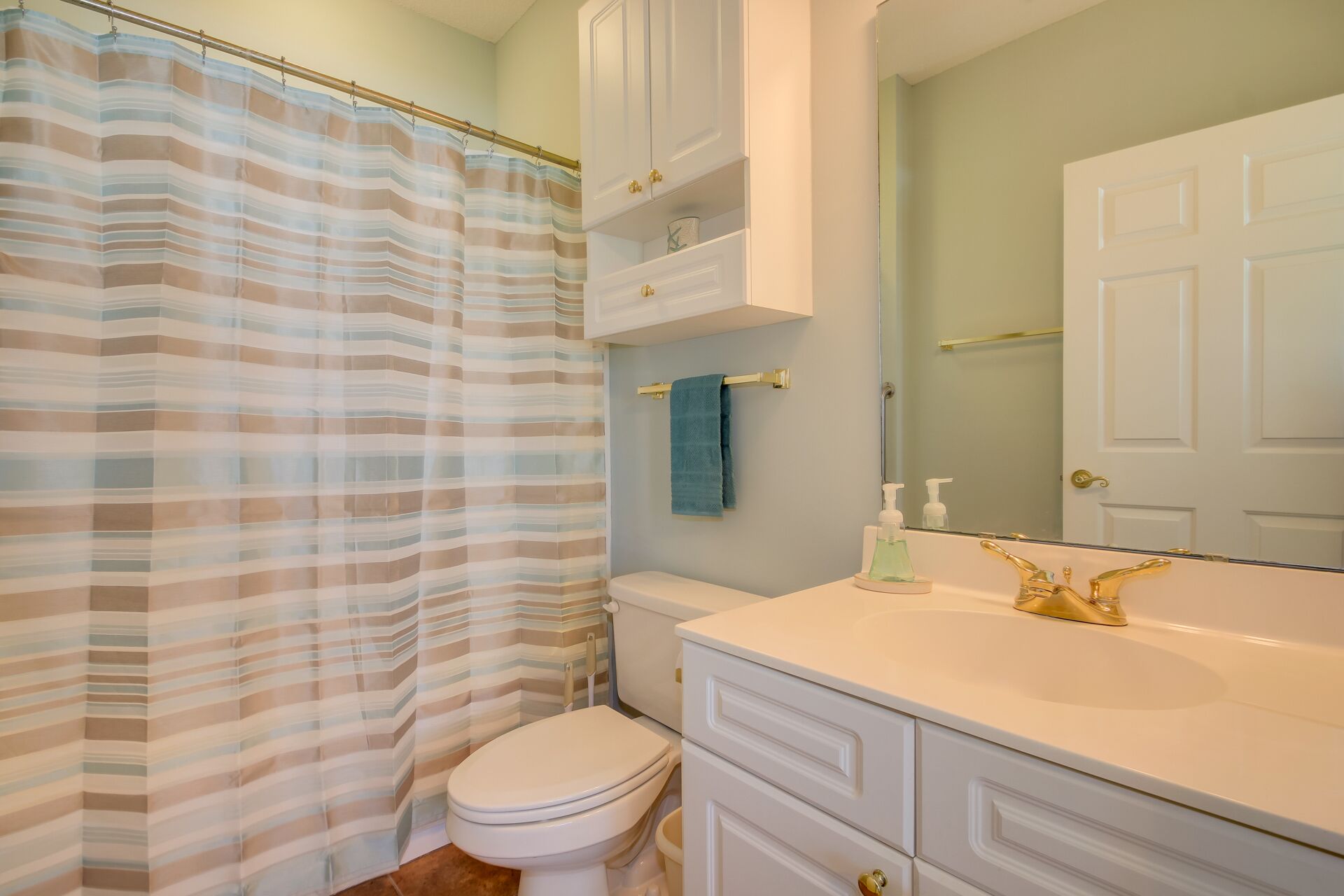 Une salle de bain avec un rideau de douche à rayures, des toilettes, un lavabo avec des robinets dorés et un miroir au-dessus du lavabo.